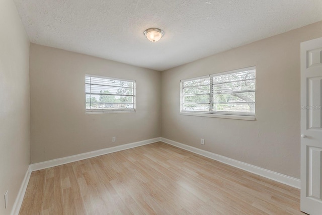 empty room with a textured ceiling, baseboards, and light wood-style flooring