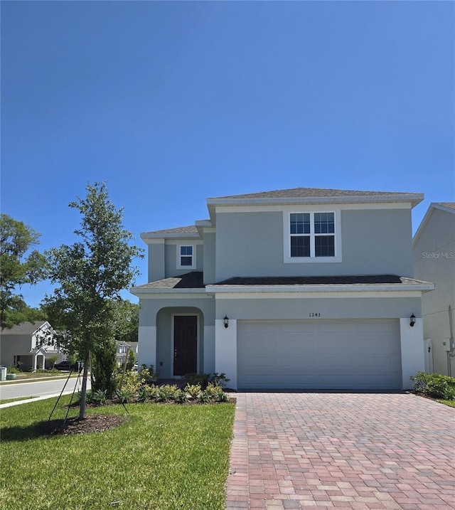 traditional-style home featuring stucco siding, an attached garage, decorative driveway, and a front lawn