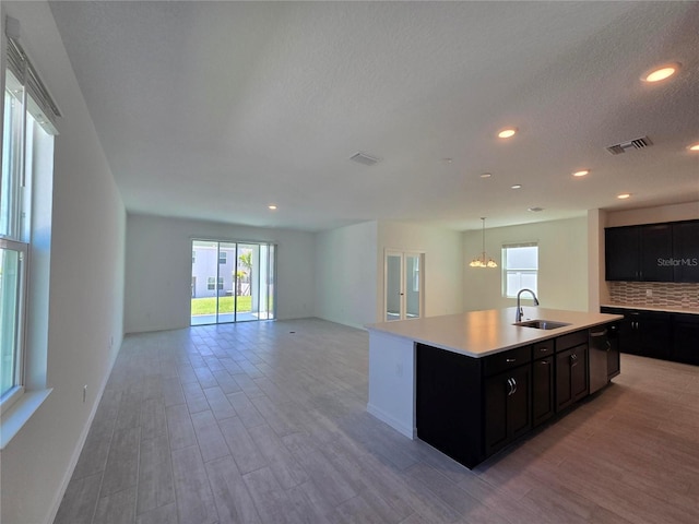 kitchen with a sink, light wood finished floors, light countertops, dark cabinets, and visible vents