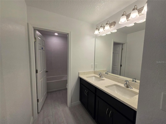 full bath featuring double vanity, wood finished floors, a textured ceiling, and a sink