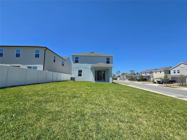 back of house with a residential view, central air condition unit, fence, a lawn, and stucco siding