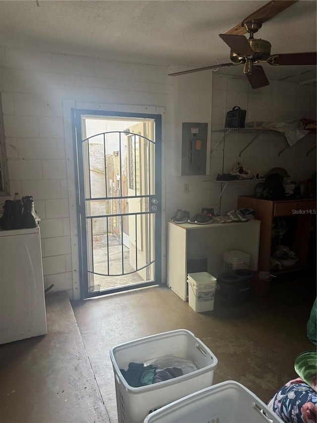 interior space featuring ceiling fan, electric panel, unfinished concrete floors, concrete block wall, and washer / dryer