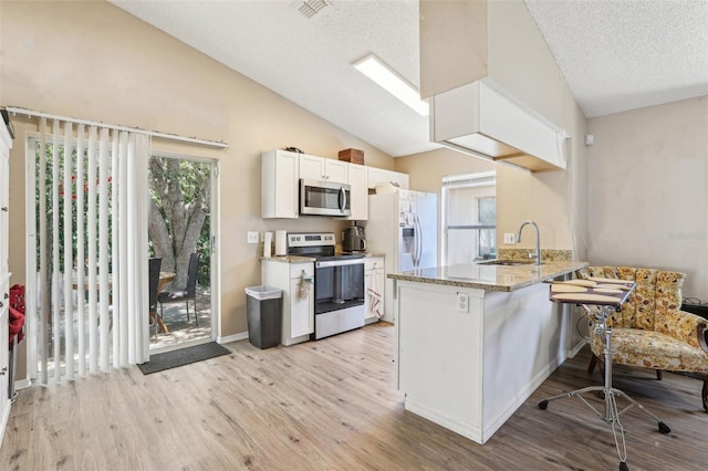 kitchen with a sink, stainless steel appliances, light wood-style flooring, a peninsula, and lofted ceiling