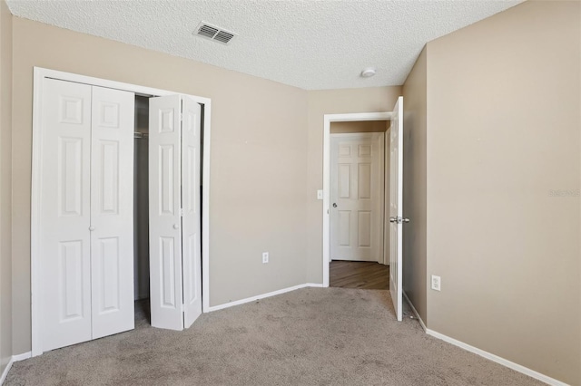 unfurnished bedroom featuring a textured ceiling, a closet, carpet, baseboards, and visible vents