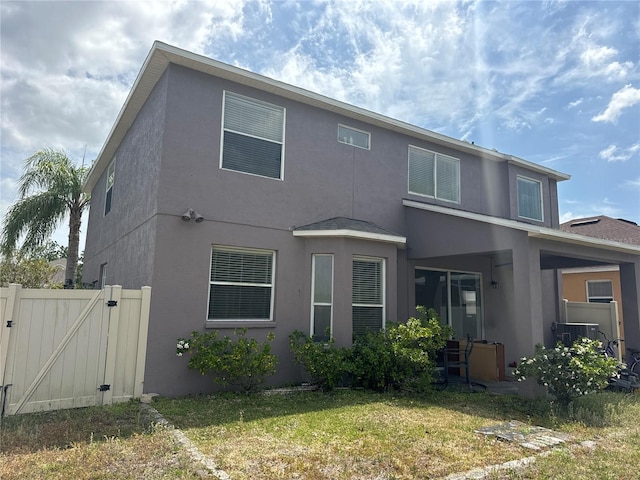 back of house featuring fence, central AC, stucco siding, a gate, and a yard