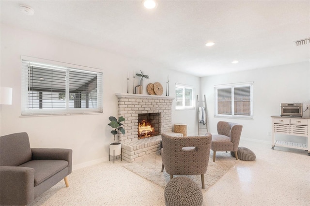 living area with a brick fireplace, visible vents, speckled floor, and baseboards