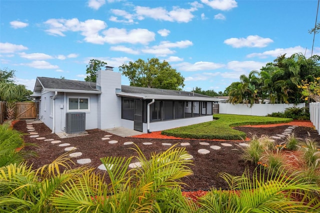 rear view of house featuring a fenced backyard, a chimney, central AC, and a sunroom