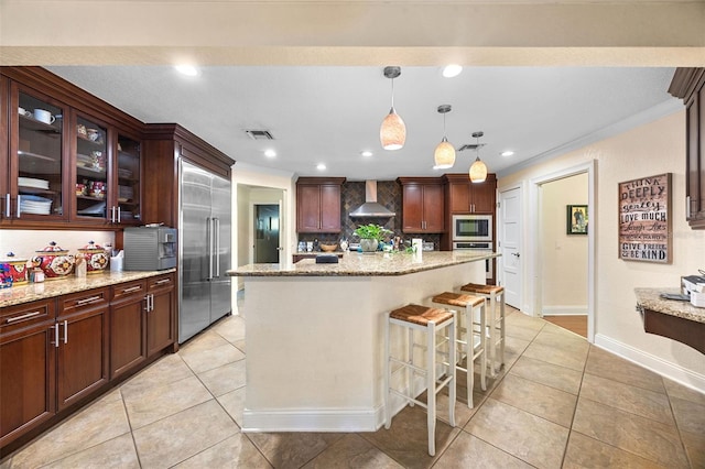 kitchen featuring built in appliances, wall chimney range hood, tasteful backsplash, and light tile patterned flooring