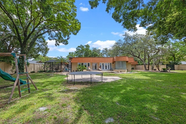 rear view of property featuring a lawn, a fenced backyard, a playground, and a trampoline