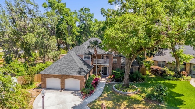 traditional-style house featuring roof with shingles, driveway, an attached garage, a balcony, and a front yard
