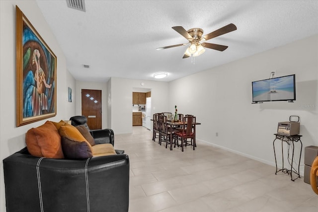 living room featuring baseboards, visible vents, a textured ceiling, and ceiling fan