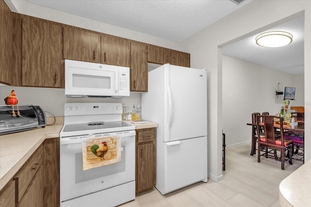 kitchen featuring a textured ceiling, brown cabinets, white appliances, a toaster, and light countertops