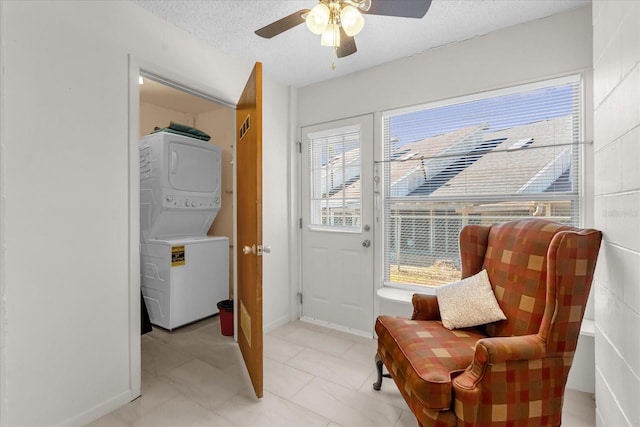 living area with baseboards, a ceiling fan, stacked washer / drying machine, and a textured ceiling