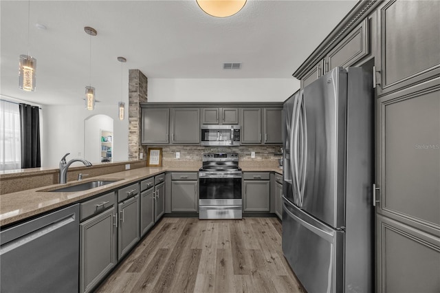 1114 Landale Ct, Orlando, FL 32828 - kitchen featuring appliances with stainless steel finishes, gray cabinetry, arched walkways, light wood-style flooring, and light stone counters