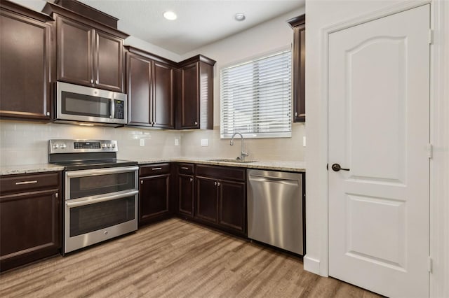 kitchen with a sink, light wood-type flooring, dark brown cabinetry, tasteful backsplash, and appliances with stainless steel finishes