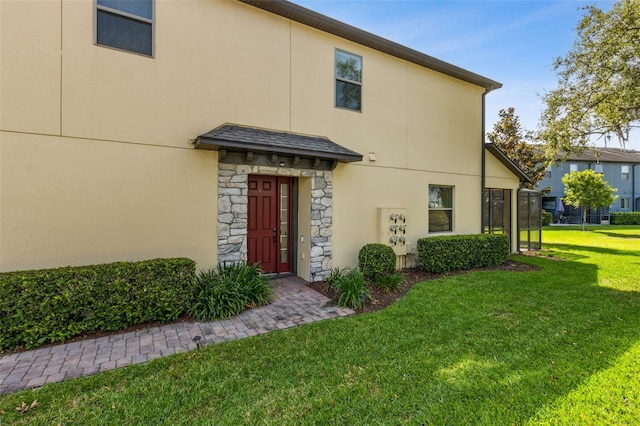back of property with stucco siding, stone siding, and a yard