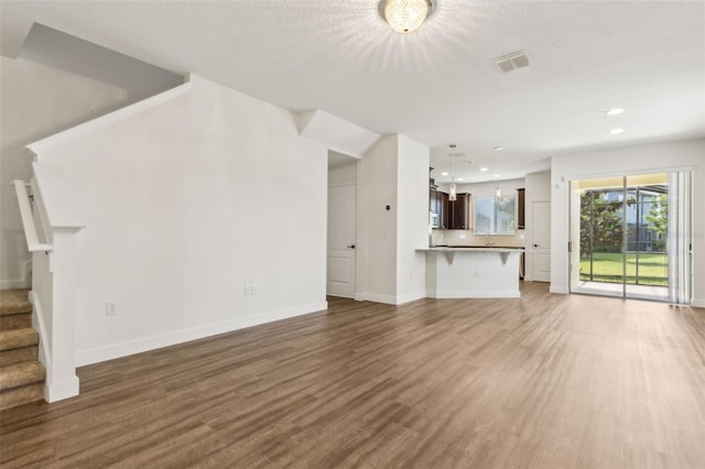 unfurnished living room with stairs, wood finished floors, baseboards, visible vents, and recessed lighting