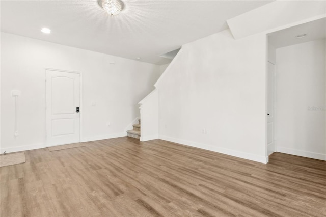 unfurnished living room featuring baseboards, stairs, light wood finished floors, and recessed lighting