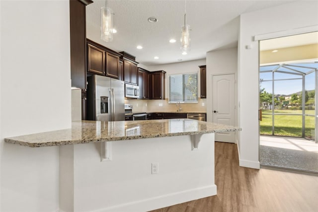 kitchen with a peninsula, light wood-style flooring, dark brown cabinetry, a breakfast bar, and appliances with stainless steel finishes