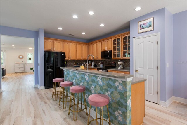 690 Cascading Creek Ln, Winter Garden, FL 34787 - kitchen featuring decorative backsplash, a kitchen island with sink, glass insert cabinets, light wood-style flooring, and black appliances