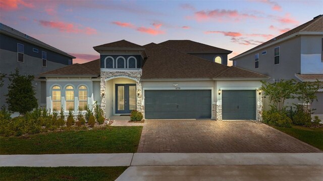 4779 Cragmere Loop, Clermont, FL 34711 - view of front of property with stone siding, decorative driveway, an attached garage, stucco siding, and french doors