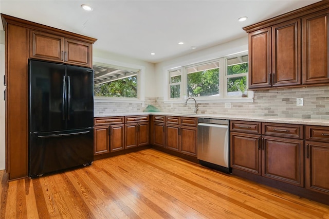 kitchen featuring dishwasher, freestanding refrigerator, light stone countertops, light wood-style flooring, and tasteful backsplash