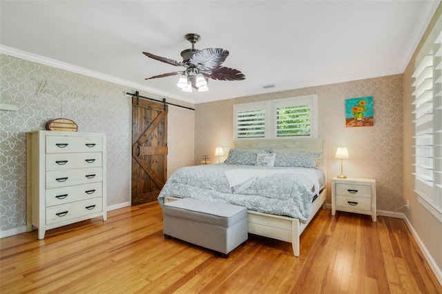 bedroom with a barn door, wallpapered walls, light wood-style floors, and ornamental molding