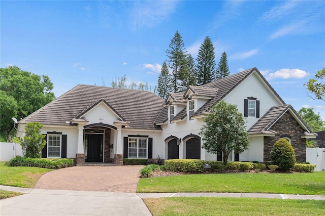 view of front facade featuring stone siding, fence, stucco siding, and decorative driveway