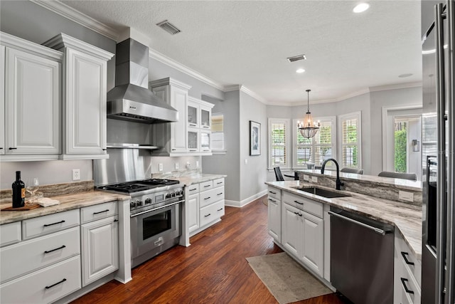 kitchen featuring wall chimney range hood, appliances with stainless steel finishes, a sink, and visible vents