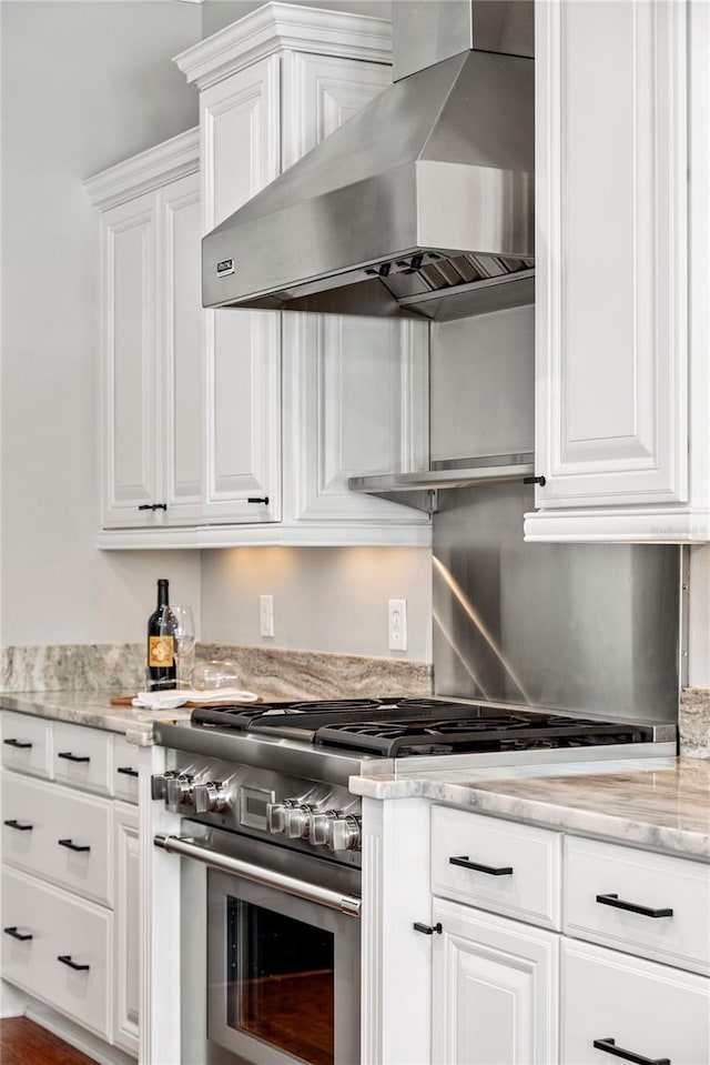 kitchen featuring wall chimney exhaust hood, stainless steel range, light stone countertops, and white cabinetry