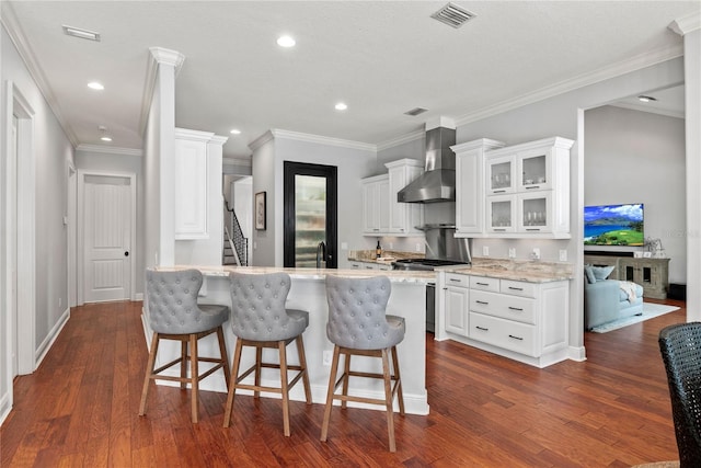 kitchen featuring wall chimney exhaust hood, a breakfast bar, visible vents, and stove