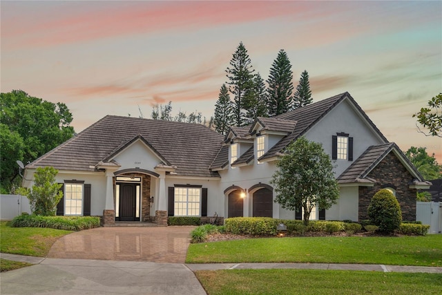 french provincial home with stone siding, fence, stucco siding, and decorative driveway