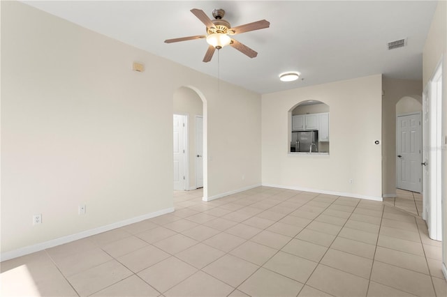 empty room featuring light tile patterned flooring, ceiling fan, arched walkways, baseboards, and visible vents