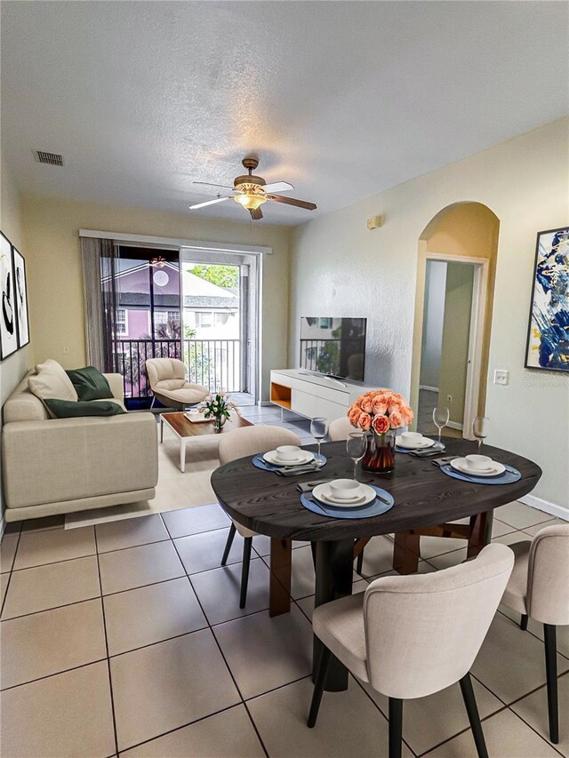 dining space featuring visible vents, a ceiling fan, light tile patterned floors, arched walkways, and a textured ceiling