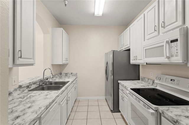 kitchen featuring white cabinets, a sink, light tile patterned flooring, white appliances, and baseboards