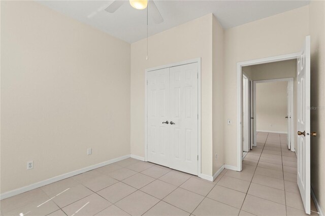 unfurnished bedroom featuring a closet, a ceiling fan, baseboards, and light tile patterned floors