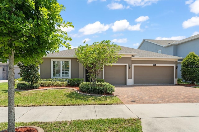 ranch-style house featuring decorative driveway, a garage, a front yard, stucco siding, and roof with shingles