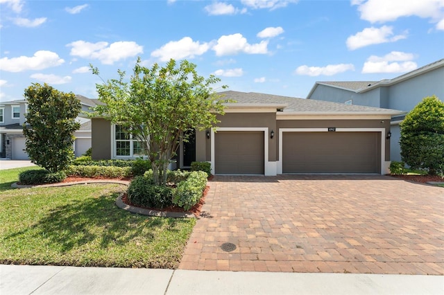 single story home featuring an attached garage, a front lawn, stucco siding, and decorative driveway