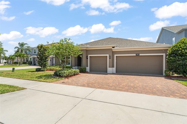 view of front of home featuring stucco siding, decorative driveway, a shingled roof, and a garage