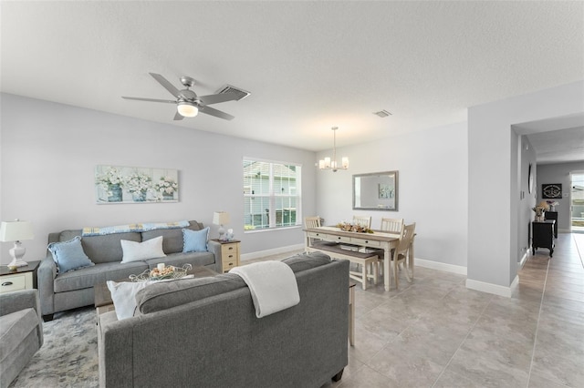 living area with ceiling fan with notable chandelier, baseboards, and a textured ceiling