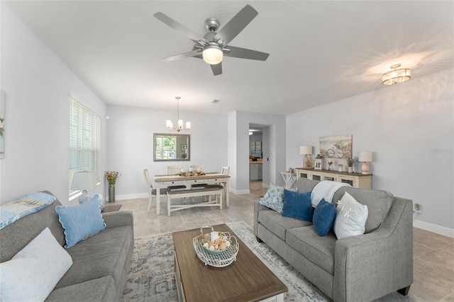 living room featuring ceiling fan with notable chandelier, baseboards, and light tile patterned floors