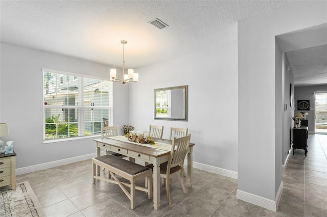 dining room with a textured ceiling, light tile patterned flooring, baseboards, visible vents, and a notable chandelier