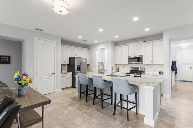 kitchen featuring stainless steel appliances, a sink, visible vents, decorative backsplash, and a breakfast bar area
