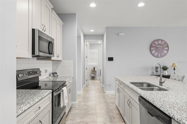 kitchen featuring a sink, baseboards, appliances with stainless steel finishes, light stone countertops, and recessed lighting