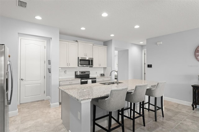 kitchen featuring visible vents, a sink, a center island with sink, appliances with stainless steel finishes, and a breakfast bar area