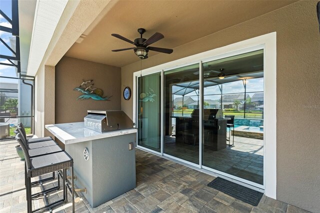 view of patio / terrace featuring glass enclosure, outdoor wet bar, an outdoor kitchen, ceiling fan, and grilling area