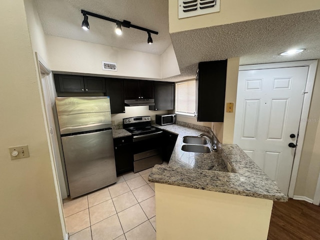 kitchen with under cabinet range hood, dark cabinetry, stainless steel appliances, and a sink