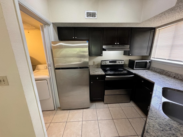kitchen with under cabinet range hood, dark cabinetry, light tile patterned floors, appliances with stainless steel finishes, and washer / clothes dryer