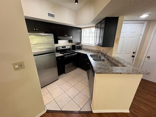 kitchen featuring under cabinet range hood, visible vents, dark cabinetry, a sink, and appliances with stainless steel finishes