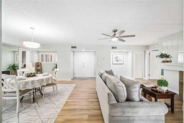 living area featuring a ceiling fan, light wood-style floors, a textured ceiling, and baseboards